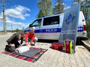 Policjanci oraz  ratownik na tle radiowozu