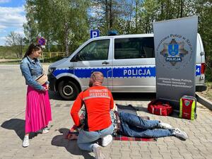 Policjanci oraz  ratownik na tle radiowozu