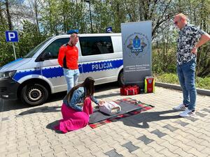 Policjanci oraz  ratownik na tle radiowozu