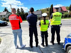 Policjanci oraz  ratownik na tle radiowozu