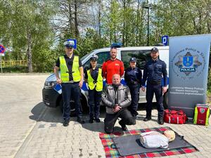 Policjanci oraz  ratownik na tle radiowozu