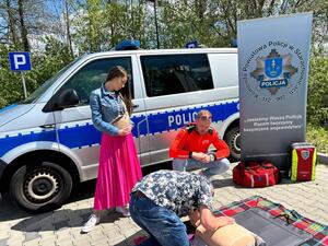 Policjanci oraz  ratownik na tle radiowozu