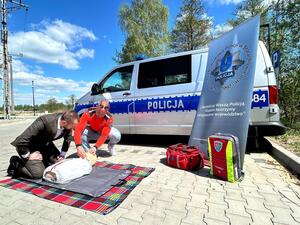 Policjanci oraz  ratownik na tle radiowozu