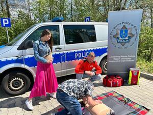 Policjanci oraz  ratownik na tle radiowozu