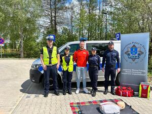 Policjanci oraz  ratownik na tle radiowozu