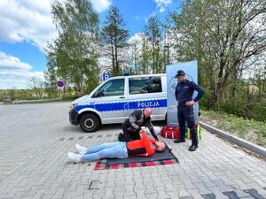 Policjanci oraz  ratownik na tle radiowozu