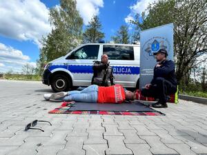 Policjanci oraz  ratownik na tle radiowozu